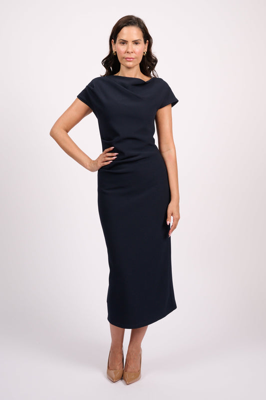A woman modeling a short-sleeve, knee-length navy blue dress with a draped neckline, standing against a light gray studio background.