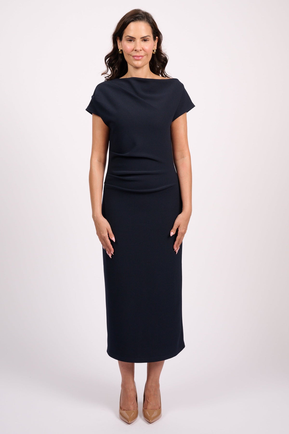 A woman modeling a dark navy midi dress with short cap sleeves, a boat neckline, and a fitted silhouette, standing against a light gray studio background.